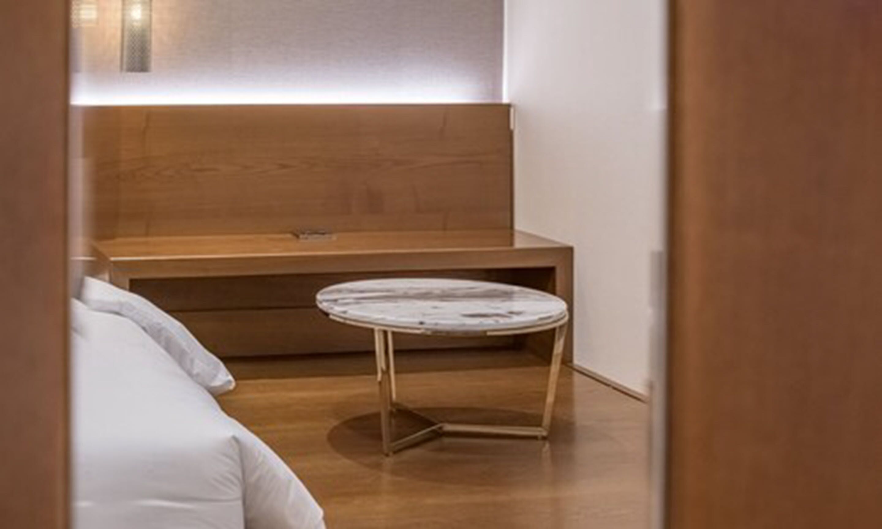 A small, modern bathroom with a wooden vanity, a round marble stool, and a white bathtub.