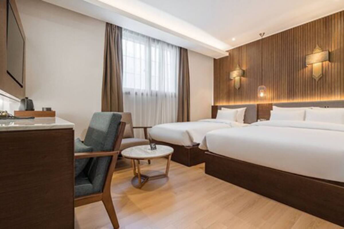 Una habitación de hotel con suelo de madera, dos camas, un escritorio, una silla y una ventana con cortinas.