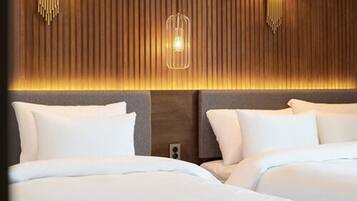 Una habitación de hotel con cabecera de madera, dos camas con ropa blanca y una lámpara colgante moderna.