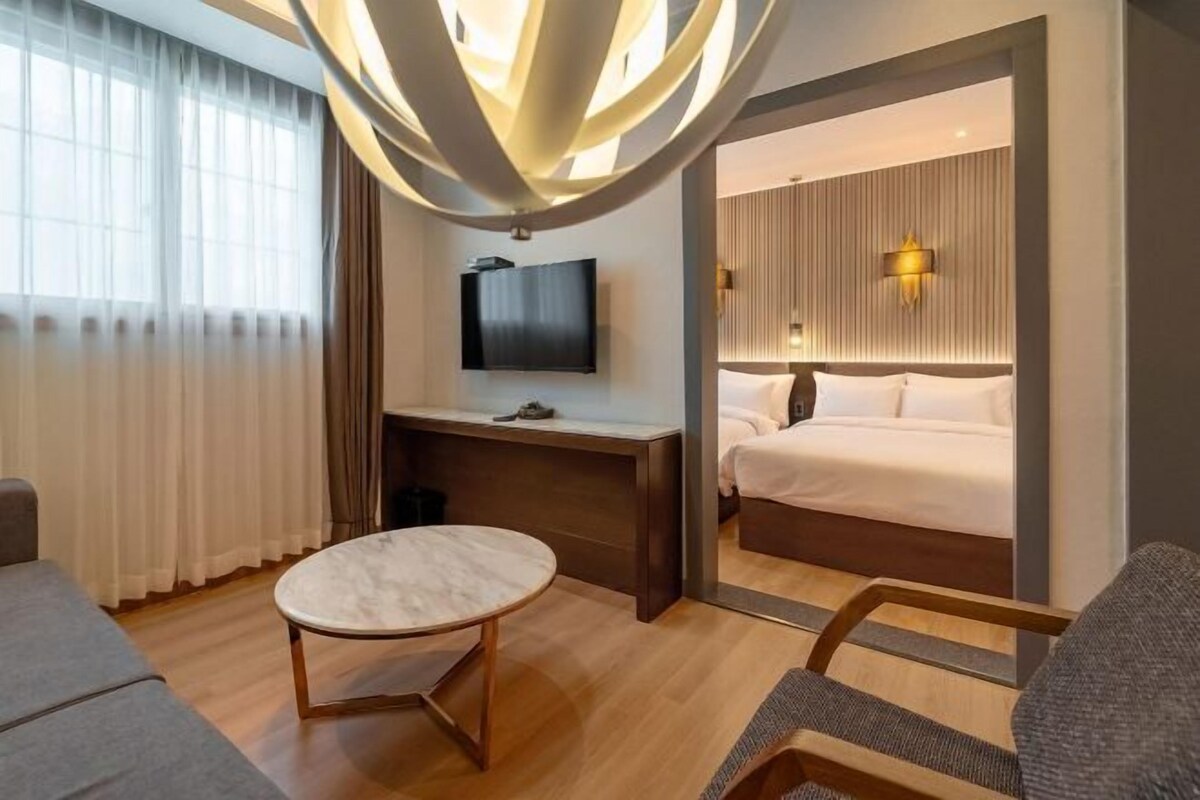 Ett modernt hotellrum med en säng, ett skrivbord, en TV och ett runt bord.