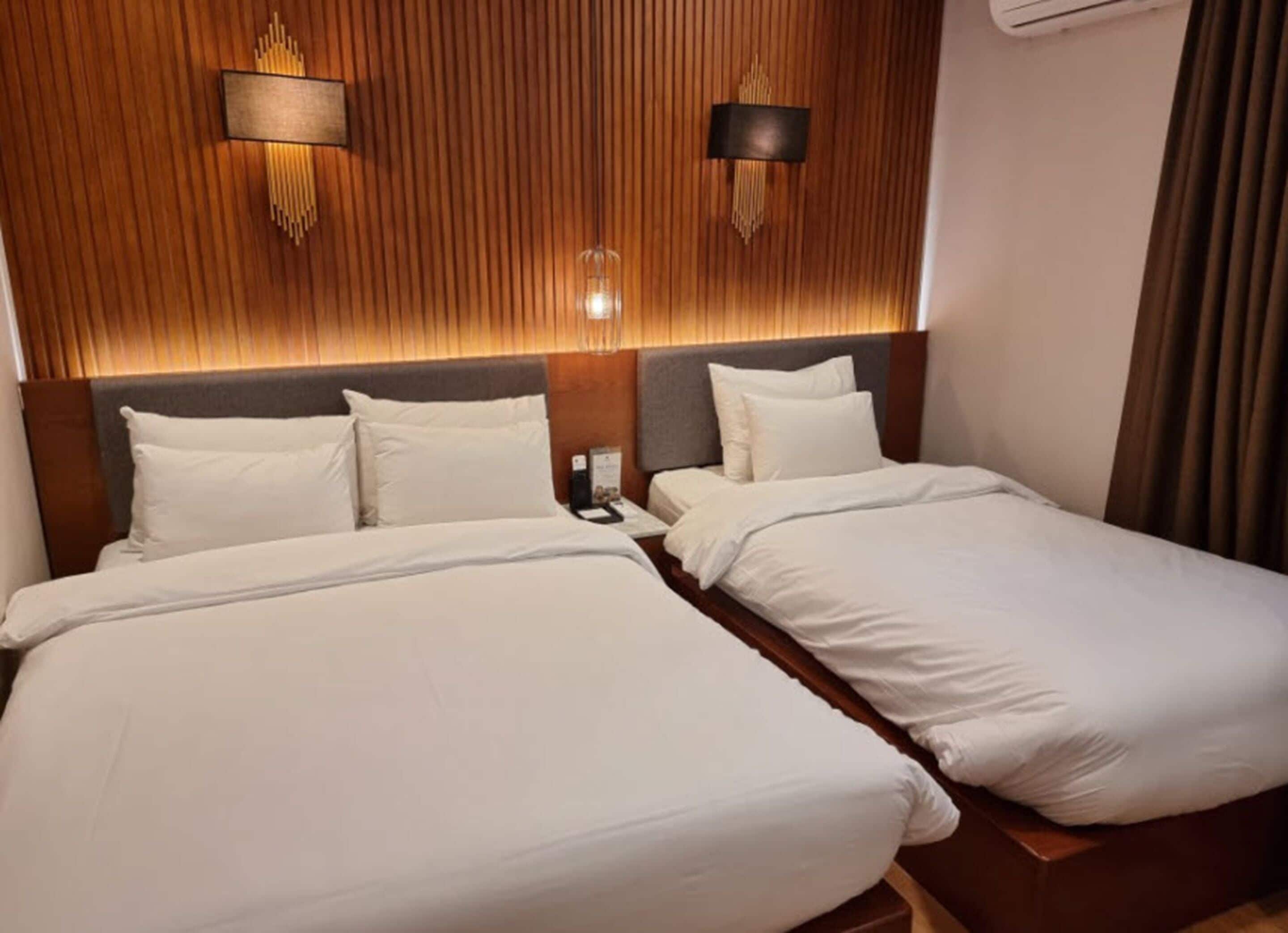 A hotel room with two single beds, wooden paneling on the walls, and two wall-mounted light fixtures.