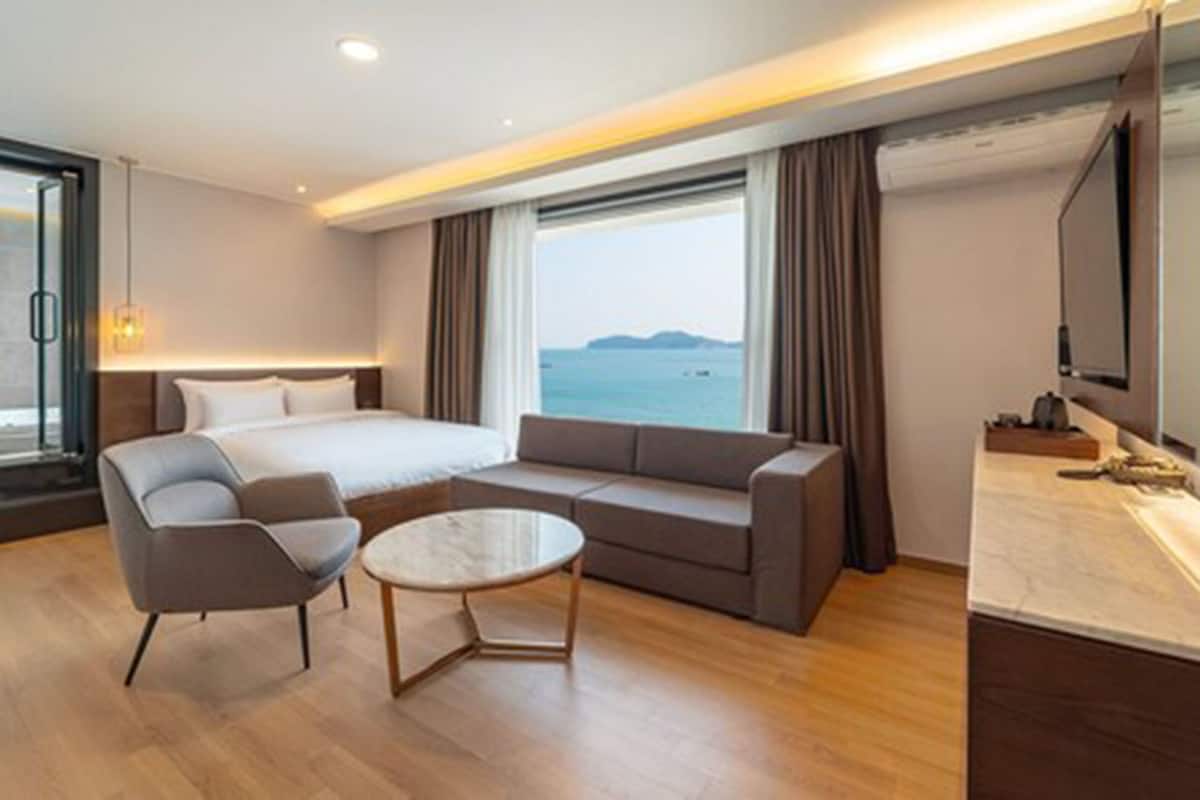 Una habitación de hotel moderna con una cama grande, un sofá, una mesita y un televisor.