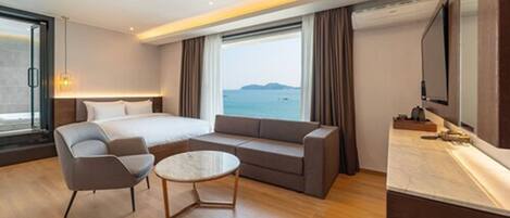 A modern hotel room with a large bed, a sofa, a small table, and a TV.