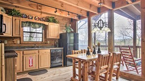 A wooden cabin kitchen with a dining table and chairs, a refrigerator, and a window overlooking a deck.