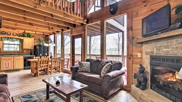 A rustic cabin interior with a fireplace, wooden furniture, and large windows.