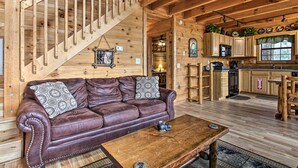 A wooden interior with a leather sofa, wooden staircase, and a kitchen area.
