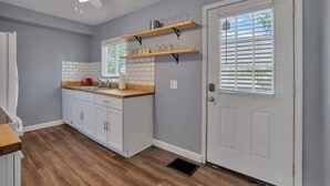 Een keuken met witte kasten, een houten aanrechtblad en een plafondventilator. Daarboven bevinden zich twee houten planken.