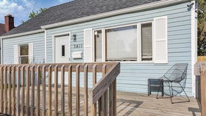 Een lichtblauwe woning met witte luiken, een houten terras en een zwarte metalen stoel.