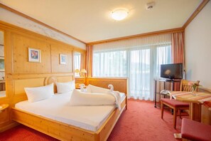 A hotel room with a wooden bed, a television, a desk, and a window with curtains. - Hotel Engel (Alberschwende)