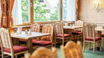 Ein Restaurant mit Holztischen und -stühlen, Blick auf Grünflächen und einer Wandleuchte.