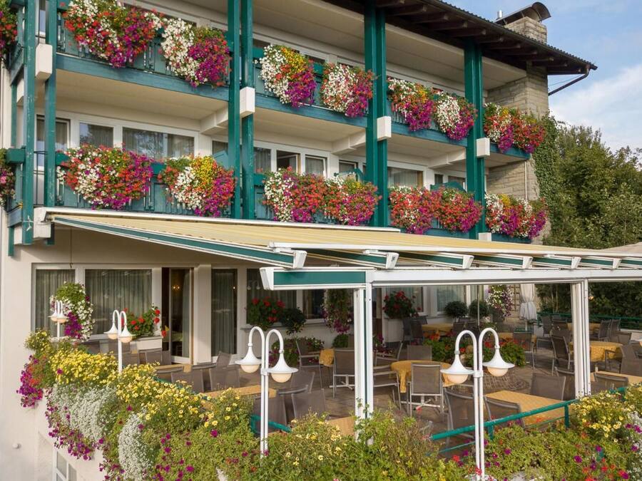 Un hotel con un área de estar al aire libre techada, varios balcones con jardineras y un cartel que indica que es un hotel.