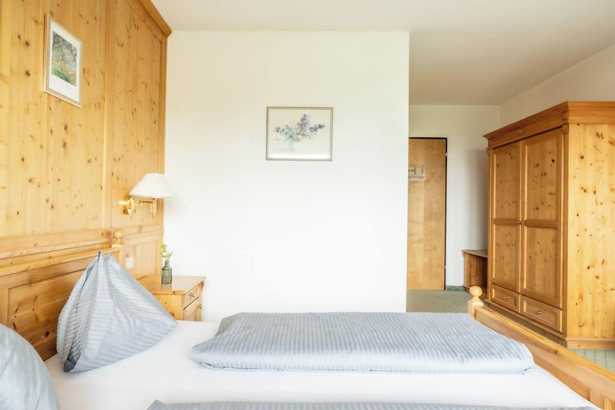 A hotel room with a wooden headboard, a bed with blue bedding, a nightstand with a lamp, a wooden wardrobe, and a framed picture on the wall.