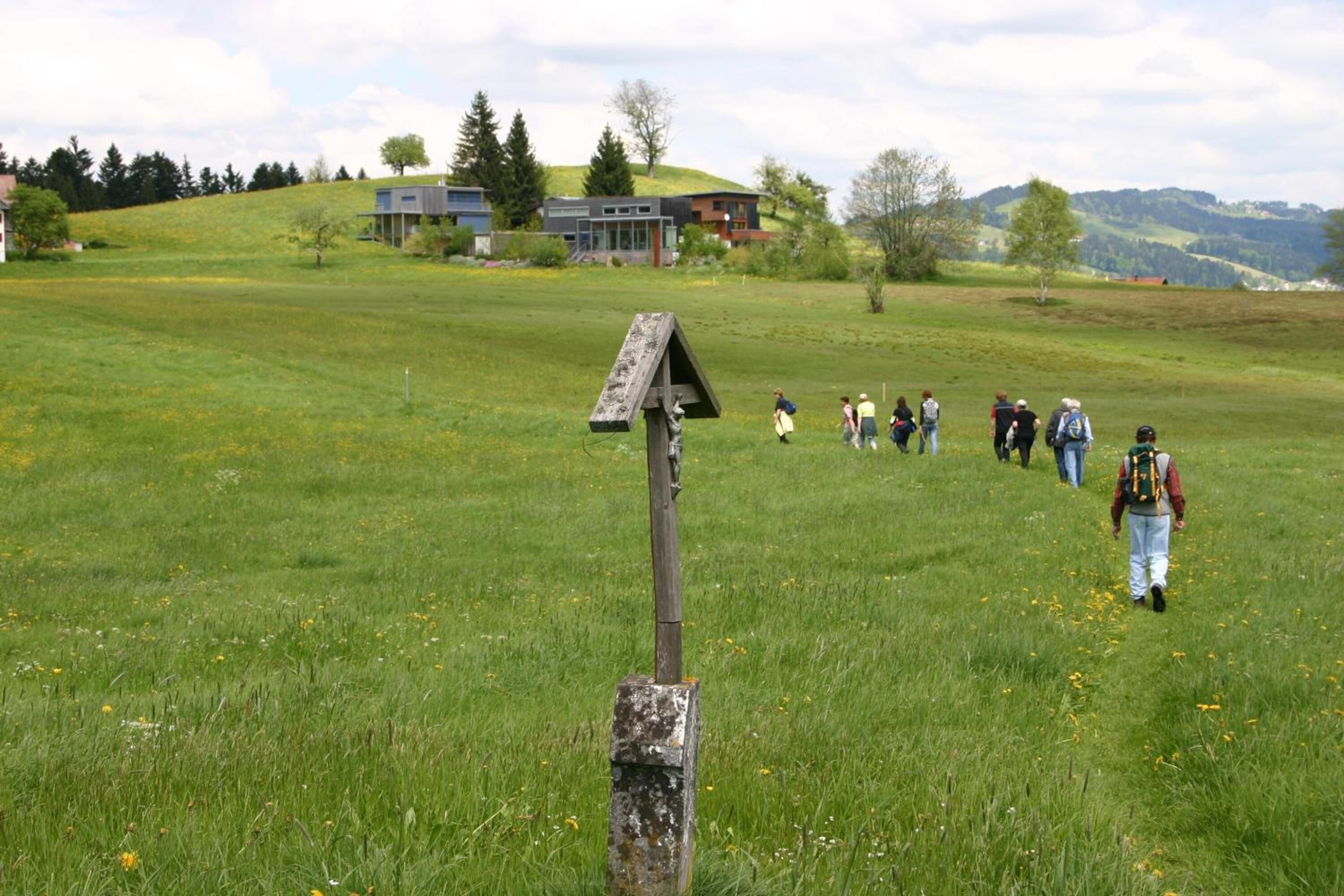 A grassy field with a wooden signpost and a group of people walking.