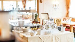 Una mesa de buffet con diversos alimentos y utensilios de servir, ubicada en una habitación con paredes de madera y una ventana.
