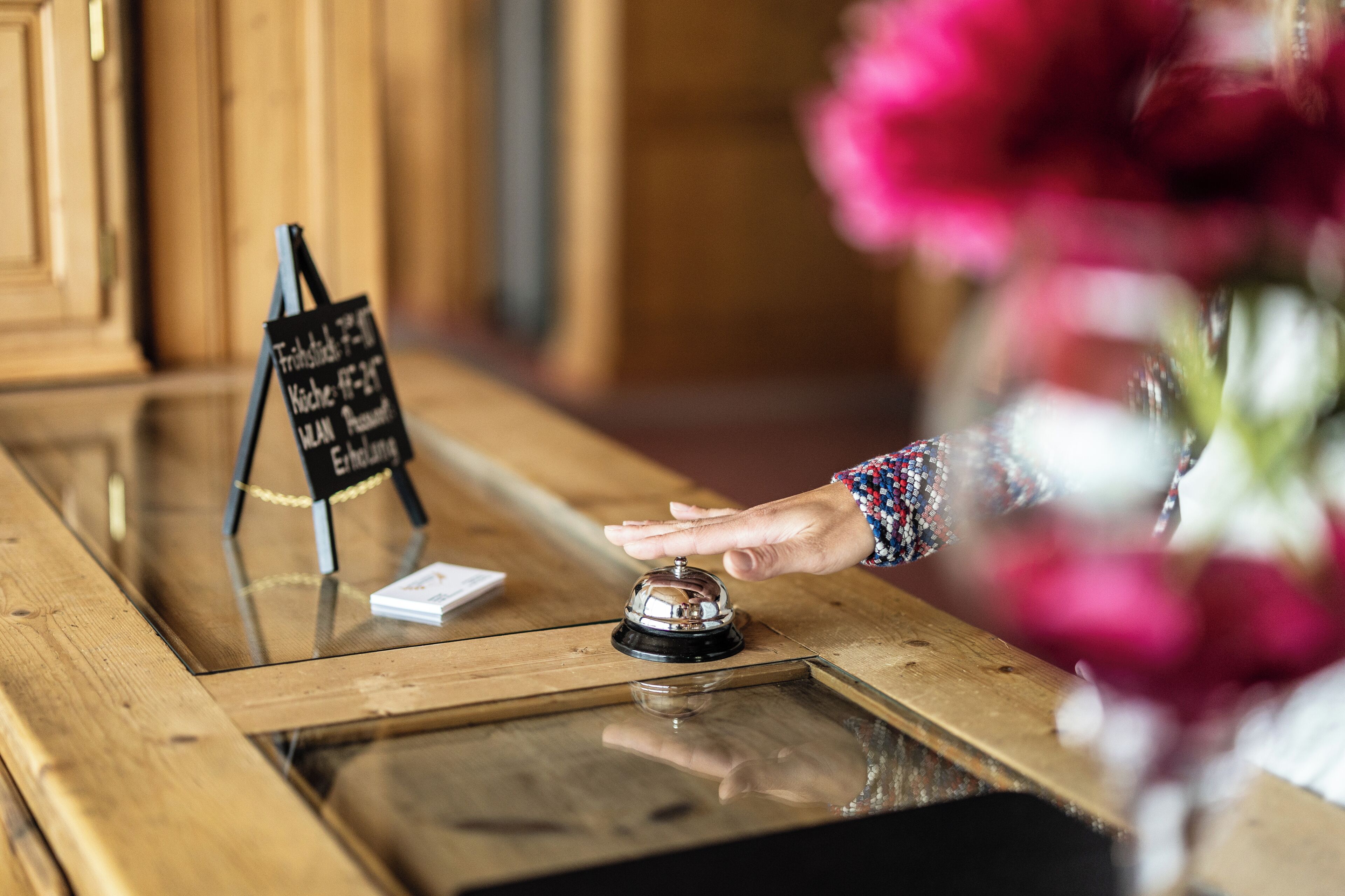 A wooden reception desk with a glass top, a bell, and a sign indicating room availability.