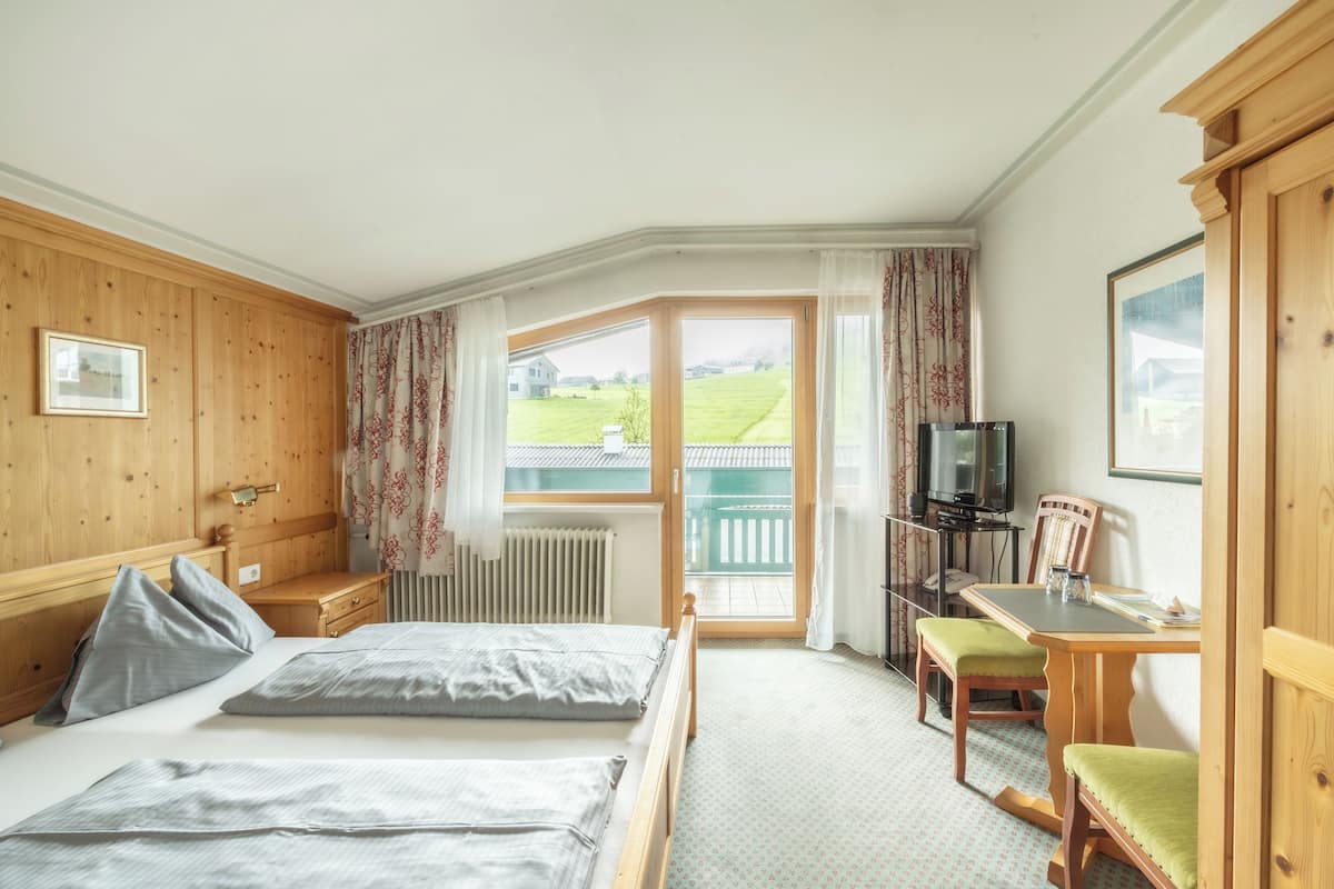 A bedroom with two beds, a desk, a chair, a television, and a view of the outdoors.
