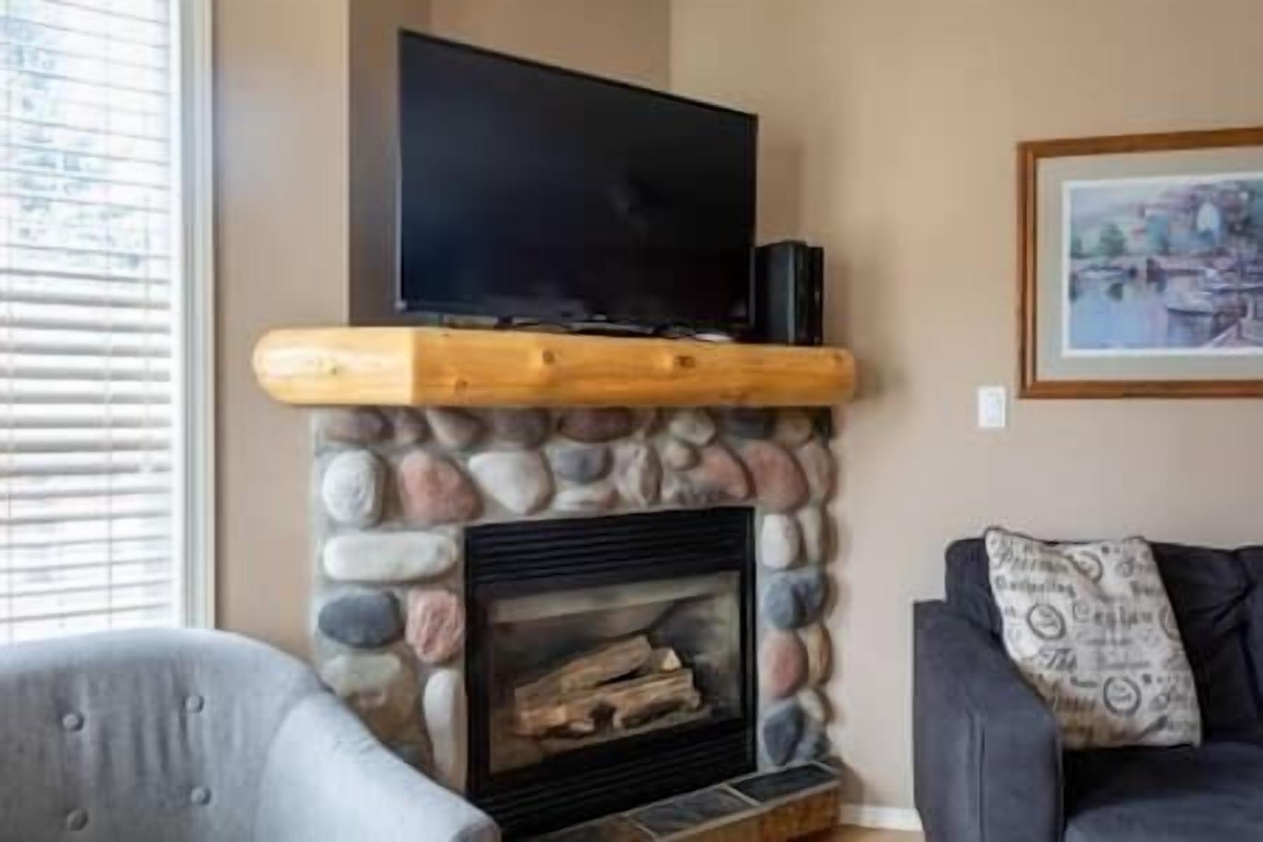 A living room with a stone fireplace, a mounted flat-screen TV, and a framed picture on the wall.