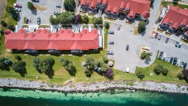 Eine Luftaufnahme eines Küstenhotels mit mehreren Gebäuden mit roten Dächern, einem Parkplatz und freiem Blick auf das türkisfarbene Meer.