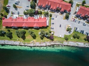 Eine Luftaufnahme eines Küstenhotels mit mehreren Gebäuden mit roten Dächern, einem Parkplatz und freiem Blick auf das türkisfarbene Meer.