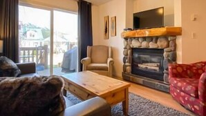 Una sala de estar con chimenea de piedra, un televisor montado encima y un puerta corrediza de vidrio que da a un área exterior.