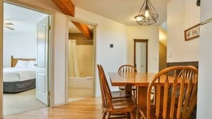 Un comedor con mesa y sillas de madera, una lámpara en el techo y una puerta que da a un dormitorio.