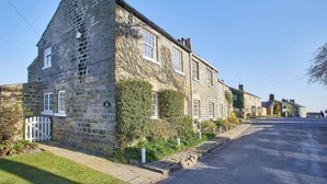 A stone building with a white picket fence, a paved driveway, and a clear sky.