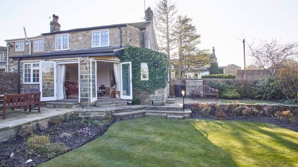 A stone house with an open front door, a bench outside, and a well-maintained lawn.