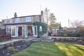 A stone house with an open front door, a bench outside, and a well-maintained lawn. - Host & Stay | Tithe Cottage (Harrogate)
