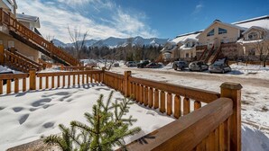 Un espace de stationnement enneigé, délimité par une clôture en bois et agrémenté d’un petit arbre à feuilles persistantes.
