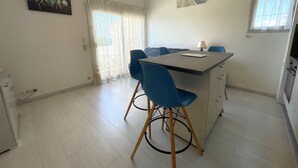 A compact dining area with a small table and blue chairs, a painting on the wall, and a window with curtains. - BANYULS-SUR-MER, A/C T2, terrace, parking, near cove (Banyuls-sur-Mer)