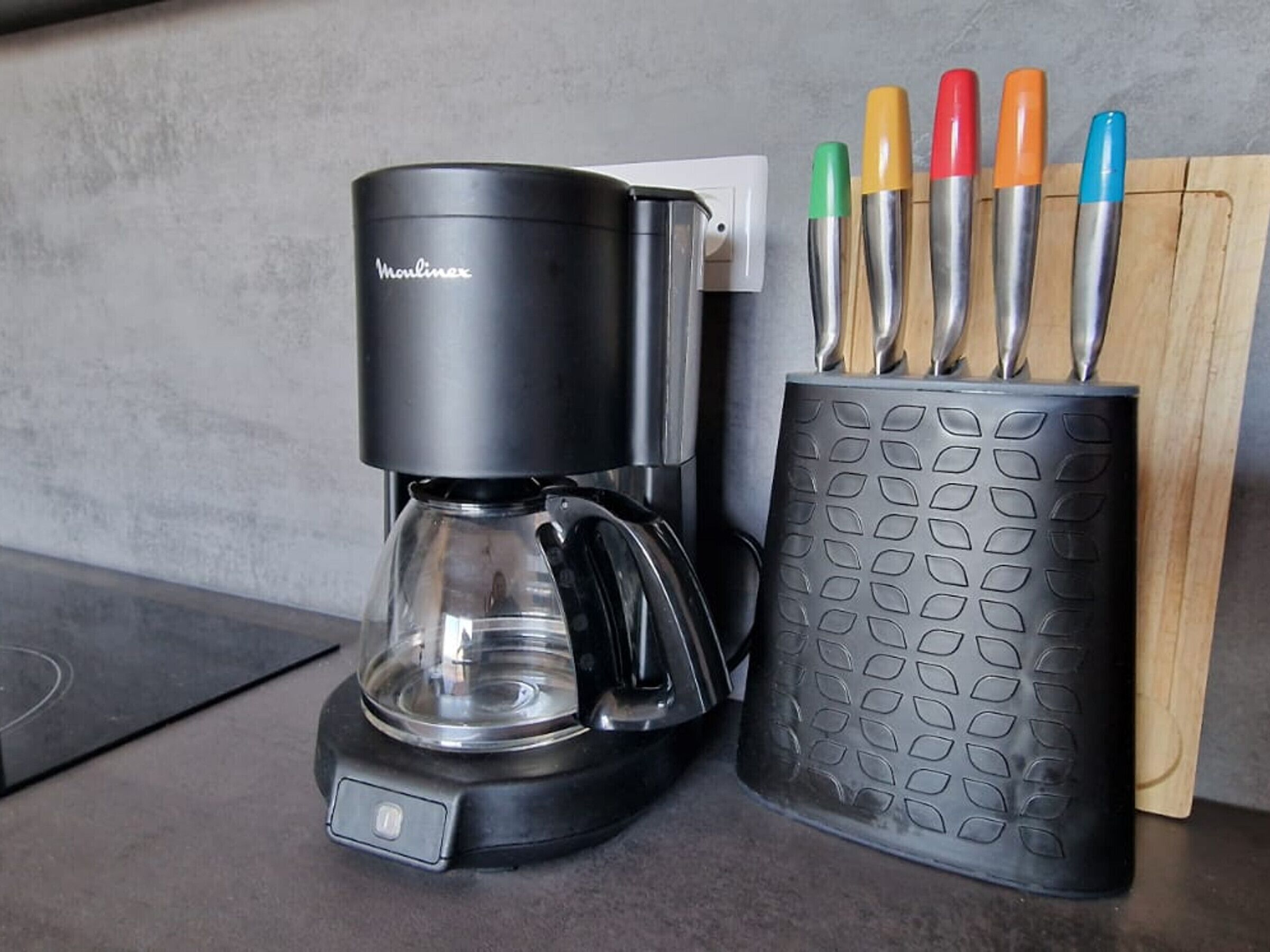 Uma cafeteira e um suporte para utensílios com talheres de diversas cores em uma bancada de cozinha.