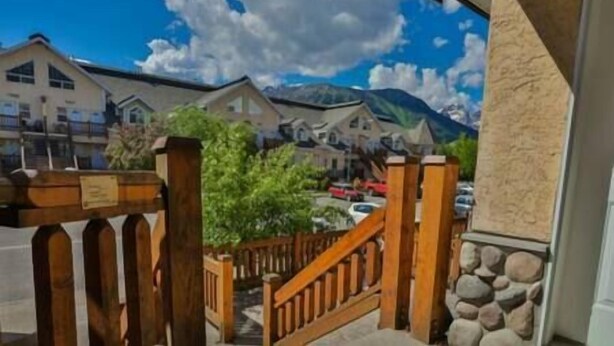 A view from a balcony with a wooden railing, overlooking a street with houses and a mountain in the background. - Spacious Townhouse / Loft Access / Mountain Views (Fernie)