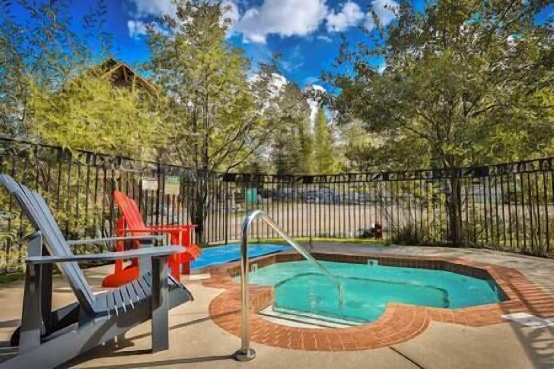 Una piscina con tobogán y una pequeña zona de deck, rodeada de una valla y árboles.