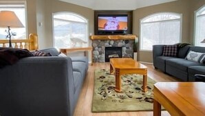 A living room with a stone fireplace, a television mounted above it, and two sofas.