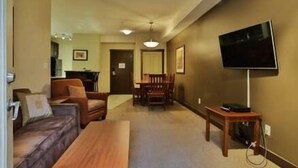 A living room with a sofa, a coffee table, a TV on a stand, and a dining area with chairs and a table.