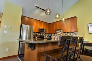 A kitchen with wooden cabinets, a stainless steel refrigerator, a microwave, and a dining area with a table and chairs. - Alpine Chalet / Hot Tub / Garage (Fernie)