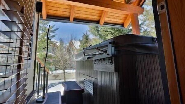 A room with a wooden ceiling, a window with blinds, a black trash bin, and a small table. - Alpine Chalet / Hot Tub / Garage (Fernie)