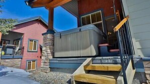 A building with a stone chimney, a porch with a wooden railing, and a staircase leading to a door. - Alpine Chalet / Hot Tub / Garage (Fernie)