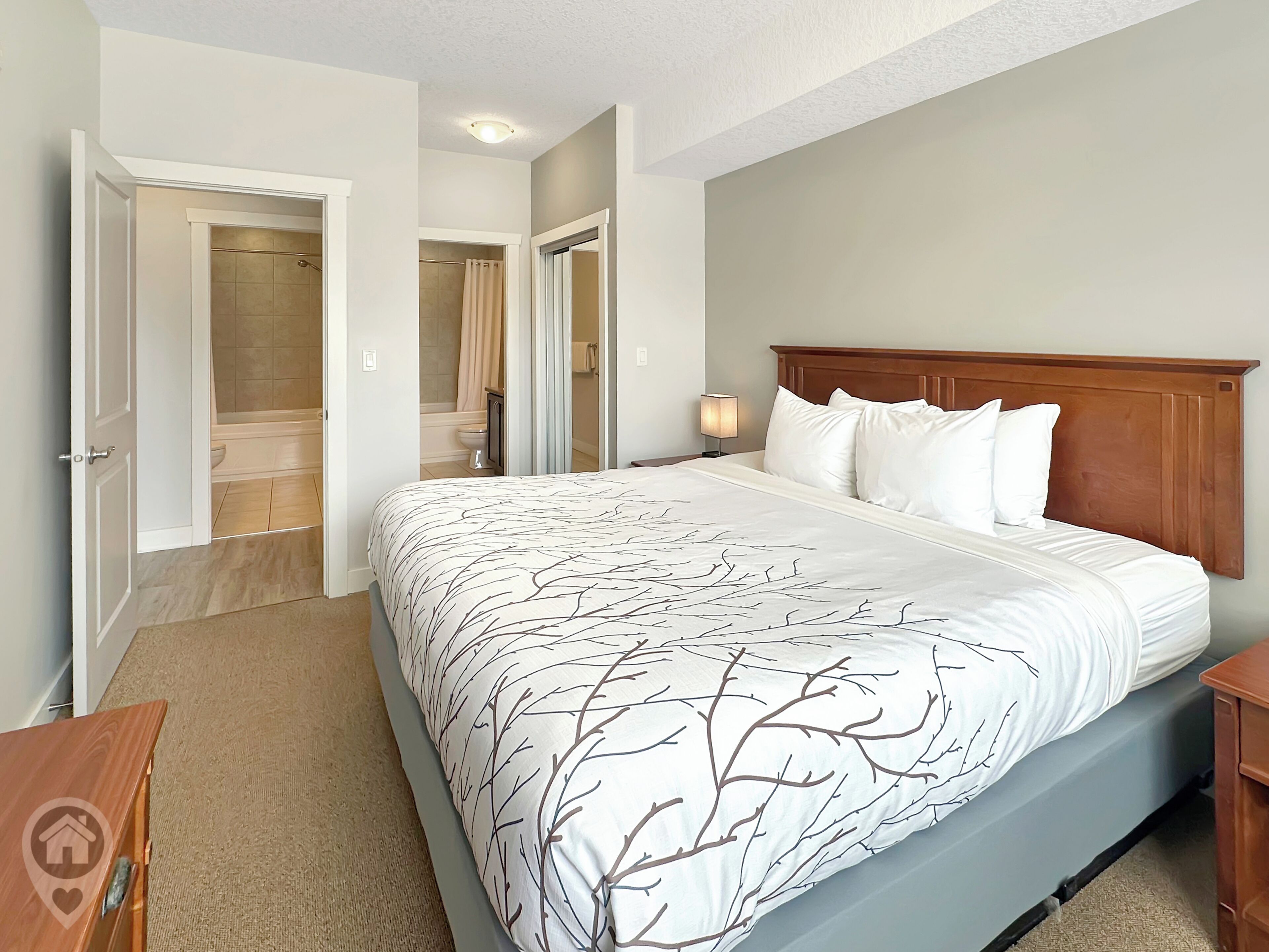 Een slaapkamer met een groot bed, een houten hoofdbord, een nachtkastje en een badkamer die door een open deur zichtbaar is.