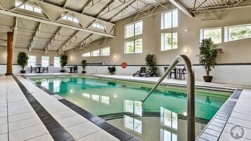 Une piscine intérieure à l’eau claire, entourée d’un sol carrelé et agrémentée de plantes en pot.