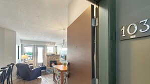 A modern interior with a dining area, kitchen, and a fireplace. - 2 BDRM / Hot Tub & Pool / AC / Fireplace (Fernie)