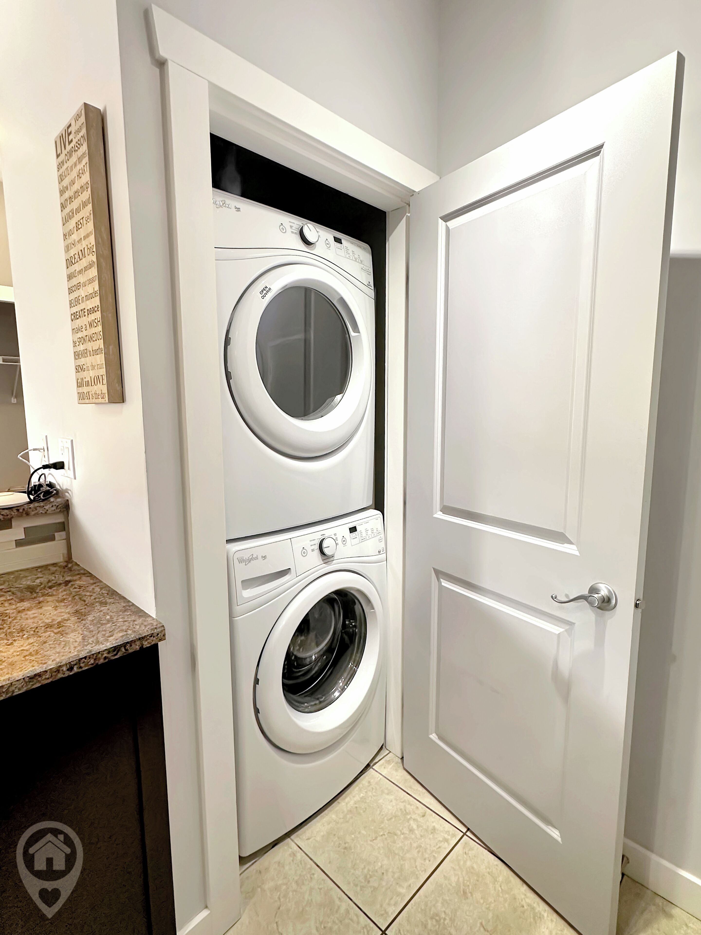A laundry room with two stacked front-loading washing machines, a countertop with a sink, and a door with a handle.