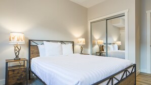 A bedroom with a large bed, two bedside tables with lamps, a wooden headboard, and a full-length mirror. - Hot Tub & Sauna / 24-Hour Check-In / Quiet (Fernie)