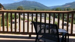 A balcony with a wooden railing overlooking a parking area and mountains in the distance.