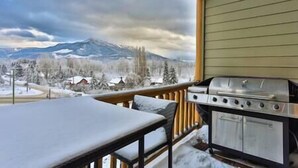 Un espace extérieur abrité, doté d’un barbecue et d’une table, offrant une vue sur un paysage enneigé et montagneux.