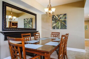 A dining room with a large mirror, wooden chairs, a glass table, and two wall-mounted paintings. - Panoramic Views! Luxury 10th Floor Condo at Sanibel Condominium #1001 (Daytona Beach Shores)