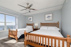 A bedroom with two wooden beds, a ceiling fan, and large windows overlooking a body of water.