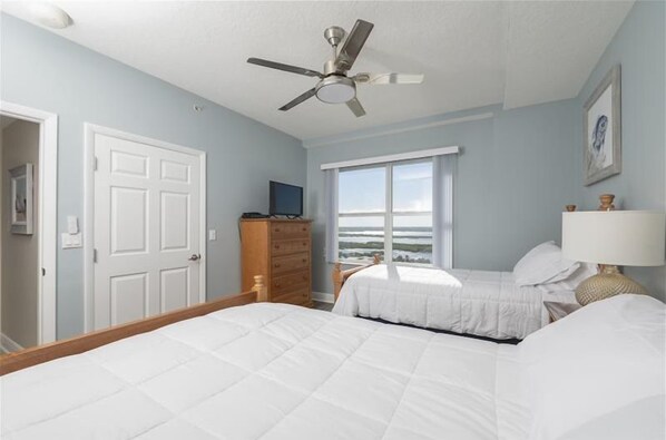 A bedroom with two beds, a ceiling fan, a dresser, a television, and a window with a view.