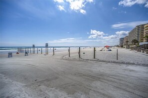 A beach with a wooden pier, sandy beach, and a building with balconies.