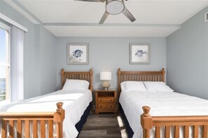 A bedroom with two wooden beds, a ceiling fan, and two framed artworks on the wall. - Panoramic Views! Luxury 10th Floor Condo at Sanibel Condominium #1001 (Daytona Beach Shores)